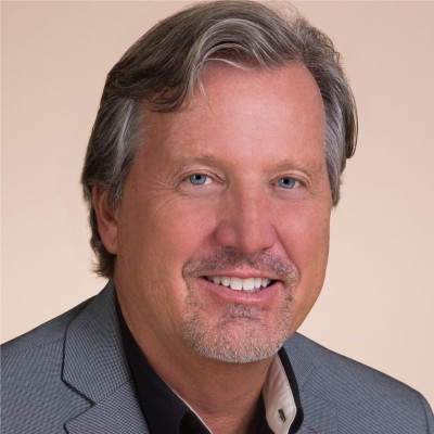 Headshot of white man with blue eyes, greying hair, and some goatee stubble in a grey suit