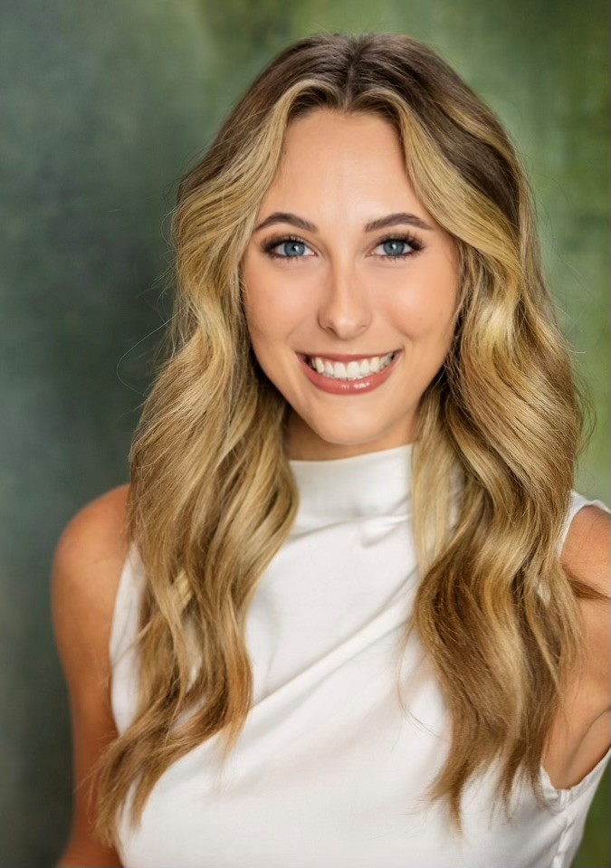 Headshot of blond white woman with blue eyes in a white sleeveless top
